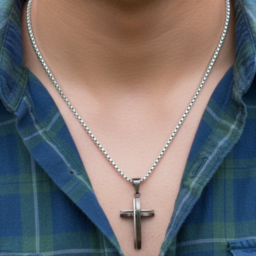 Male model chest up wearing square box chain with layered bicolor cross and plaid shirt